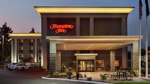 Un hôtel Hampton Inn doté d’une façade moderne, d’une entrée bien éclairée et d’un parking où sont stationnées des voitures.