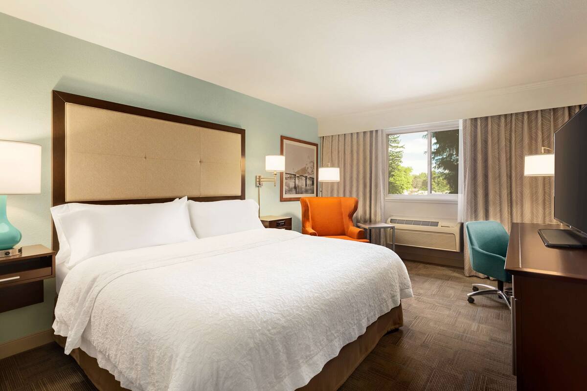 A hotel room with a large bed, a desk, an orange chair, and a television.