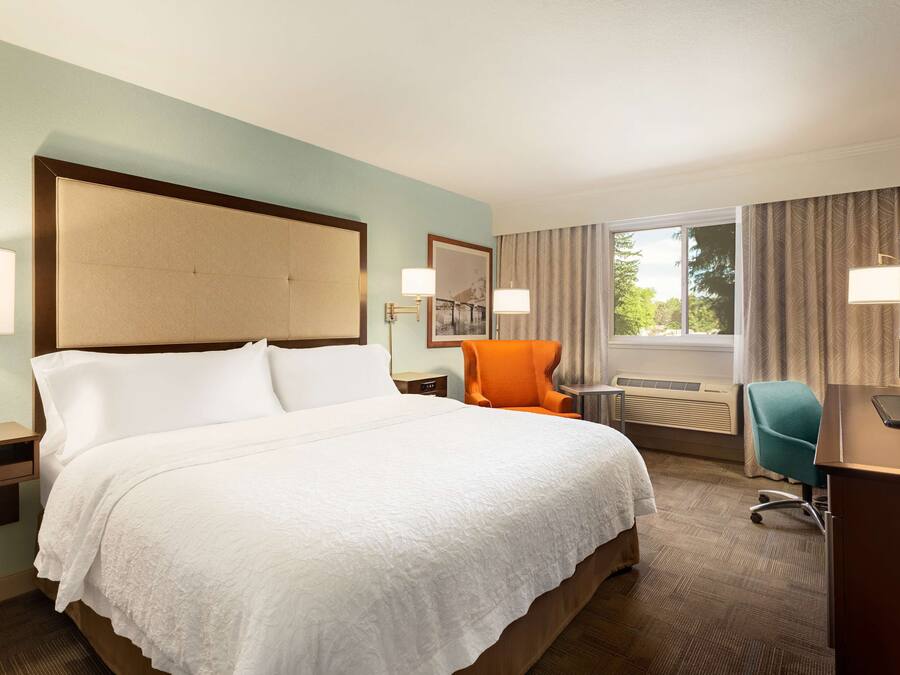 A hotel room with a large bed, a desk, an orange chair, and a television.