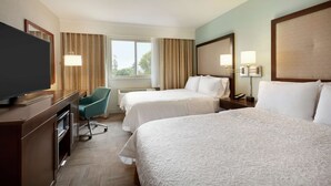 Une chambre d’hôtel avec deux lits, un bureau avec une télévision, une chaise et une fenêtre avec des rideaux.