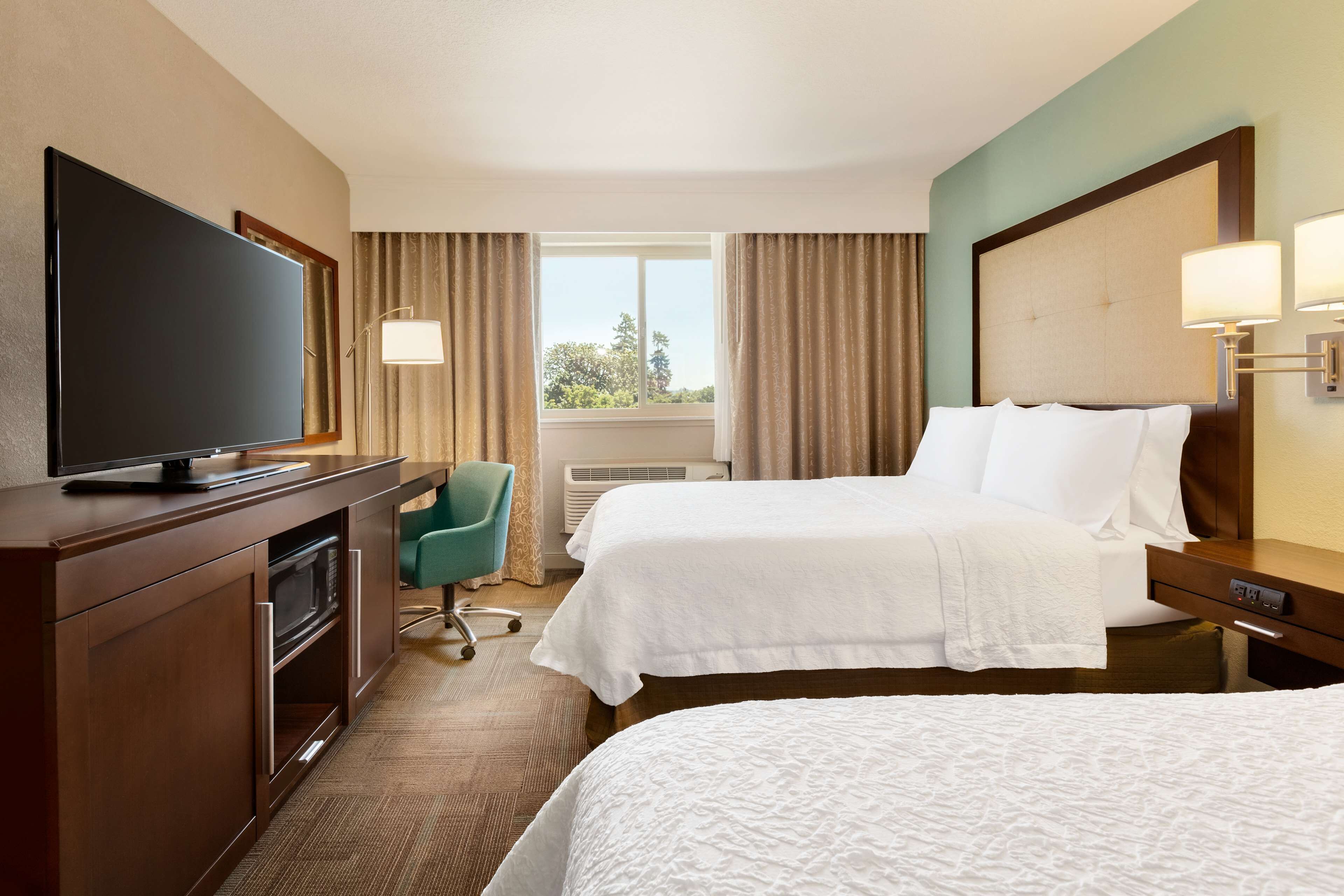 A hotel room with two beds, a TV, a desk, and a chair.