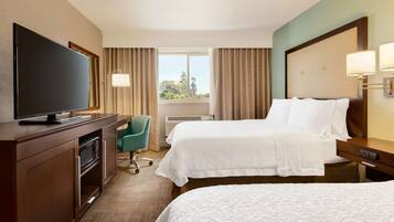 A hotel room with two beds, a TV, a desk, and a chair.