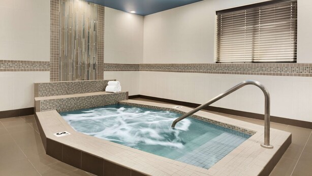 Une salle de spa moderne dotée d’un jacuzzi, de murs carrelés et d’une fenêtre avec stores.