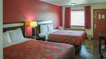 A hotel room with two beds, a nightstand, a lamp, and a window with curtains.