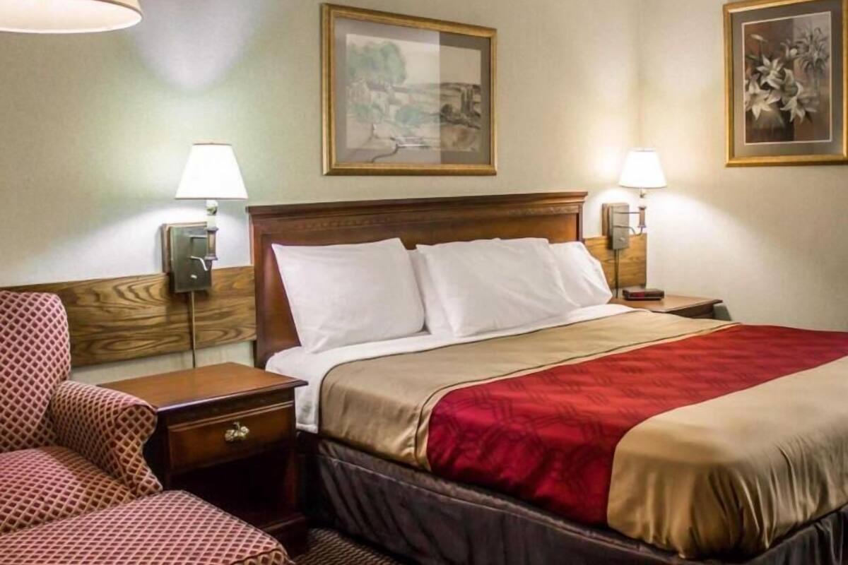A hotel room with a bed, nightstands, a lamp, a chair, and two framed pictures on the wall.