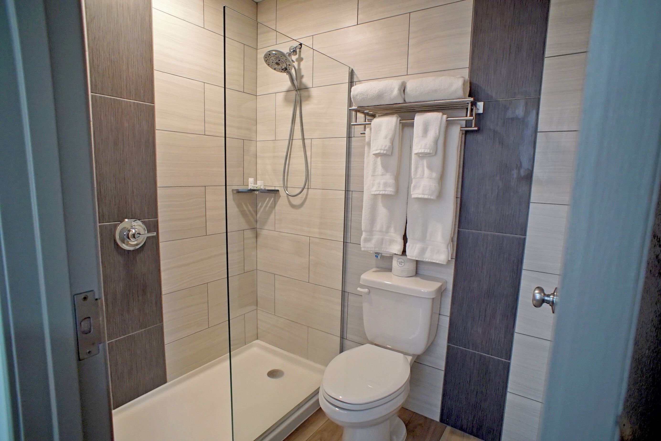 A modern bathroom with a glass-enclosed shower, a white toilet, and a towel rack with multiple towels.