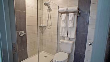 A modern bathroom with a glass-enclosed shower, a white toilet, and a towel rack with multiple towels.