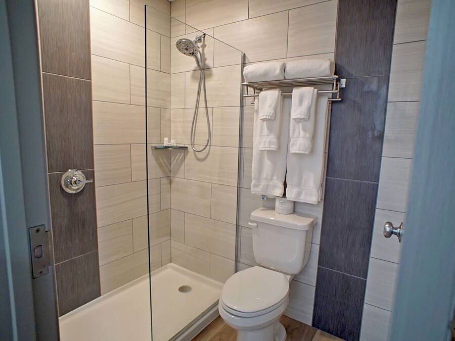 Une salle de bain moderne avec une douche à parois de verre, des toilettes blanches et un porte-serviettes avec plusieurs serviettes.