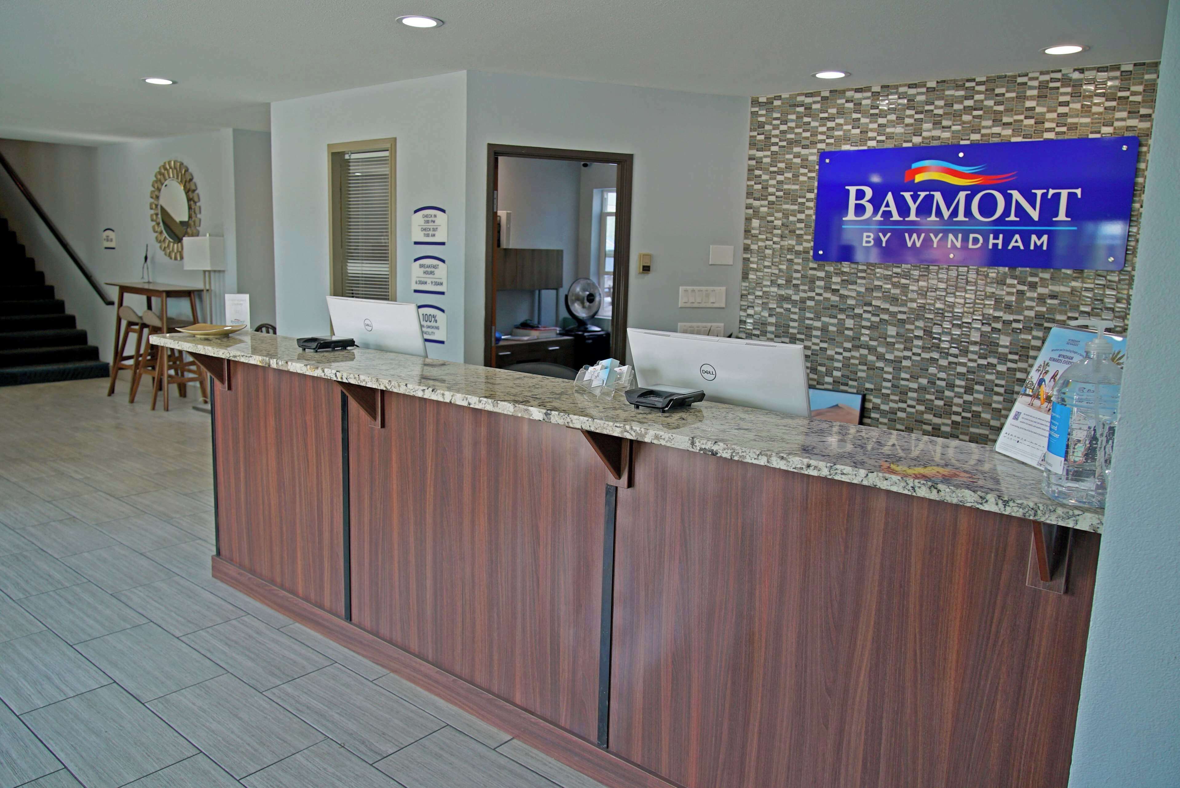 A reception desk with a sign reading "Baymont by Wyndham," a computer, and a mirror.