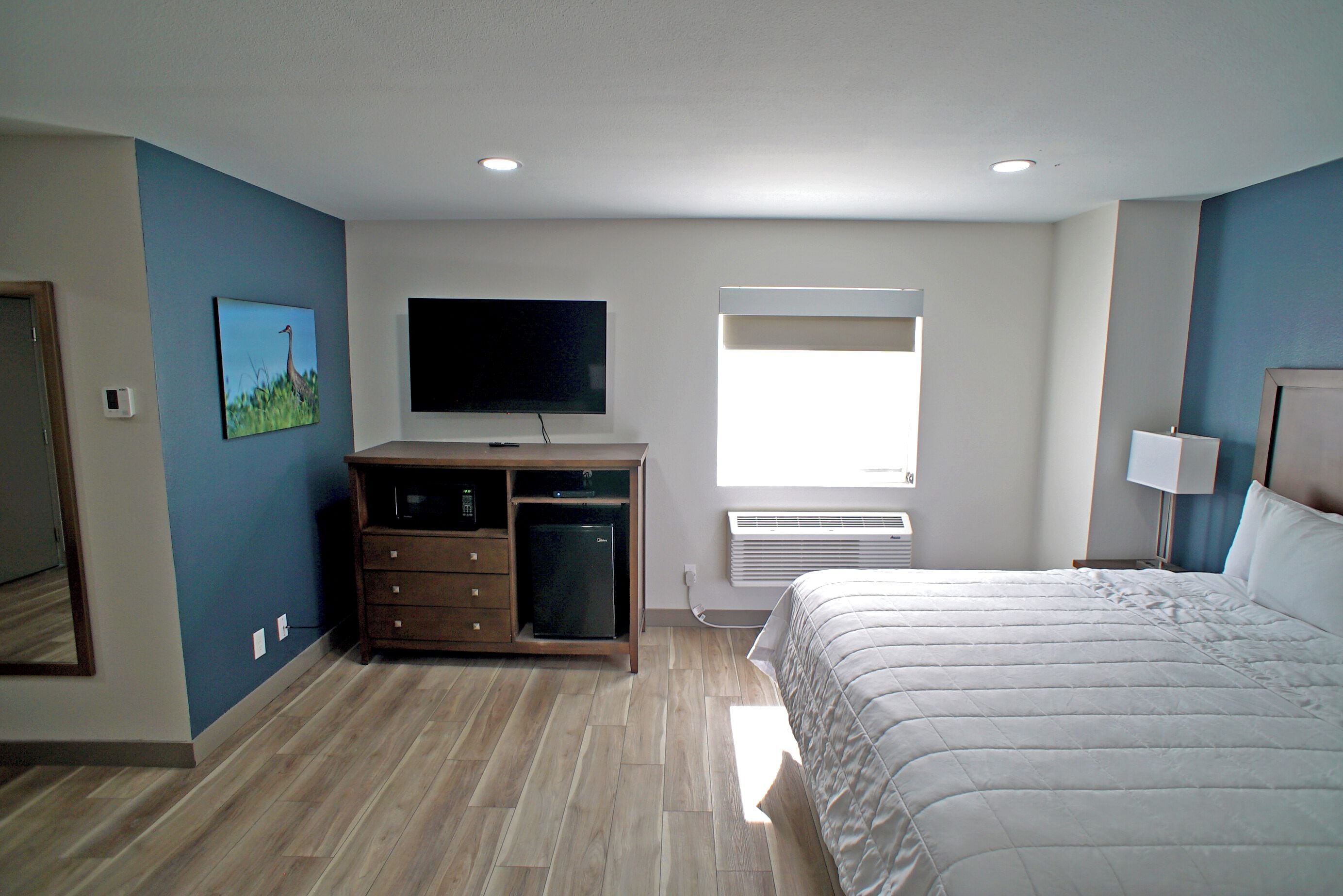 A bedroom with a bed, a TV, a small fridge, and a window.