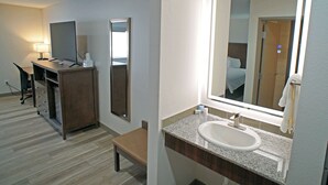 A hotel bathroom with a sink, mirror, and a desk with a chair. - Baymont | Monte Vista (Monte Vista)