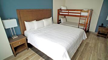 Habitación de hotel con una cama grande, una cama individual en una litera, una mesita de noche con una lámpara y piso de madera.