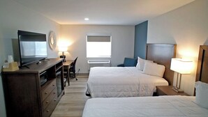 A hotel room with two beds, a desk with a chair, a television, and a wall-mounted mirror.
