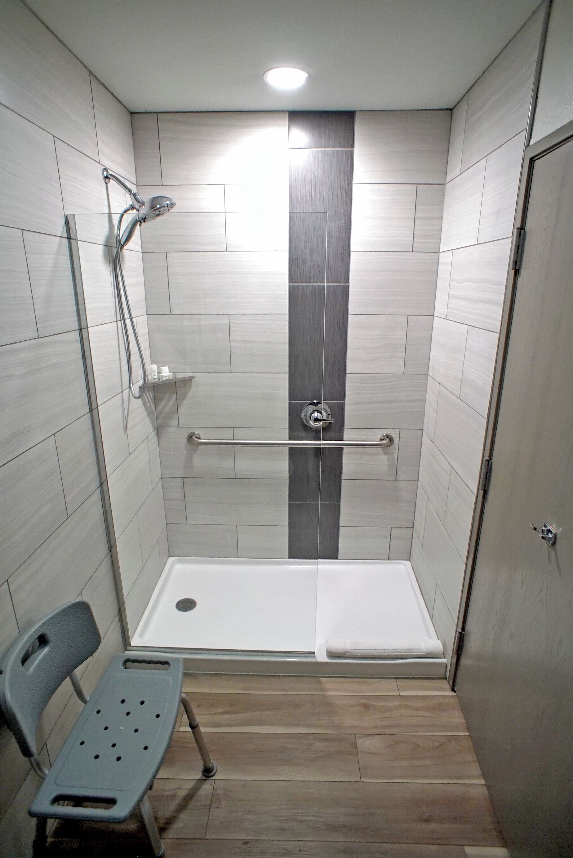 A shower stall with a bench, a handrail, and a tiled wall.