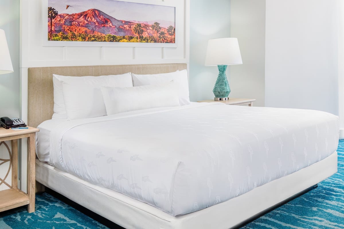 Habitación de hotel con una cama grande, dos mesitas de noche, un cuadro en la pared y una alfombra azul.