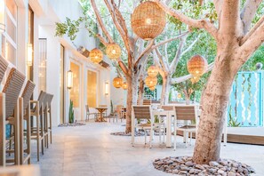 A tree with hanging lanterns, wooden chairs, and tables arranged in an outdoor seating area. - Riviera Resort Palm Springs (Palm Springs)
