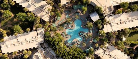 Vista aérea de un resort con piscina central, rodeado de zonas de descanso y palmeras.