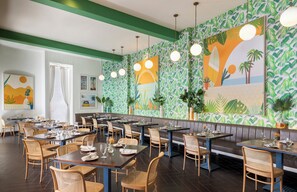 A restaurant with a tropical theme, featuring green and white patterned walls, wicker furniture, and pendant lighting. - Riviera Resort Palm Springs (Palm Springs)