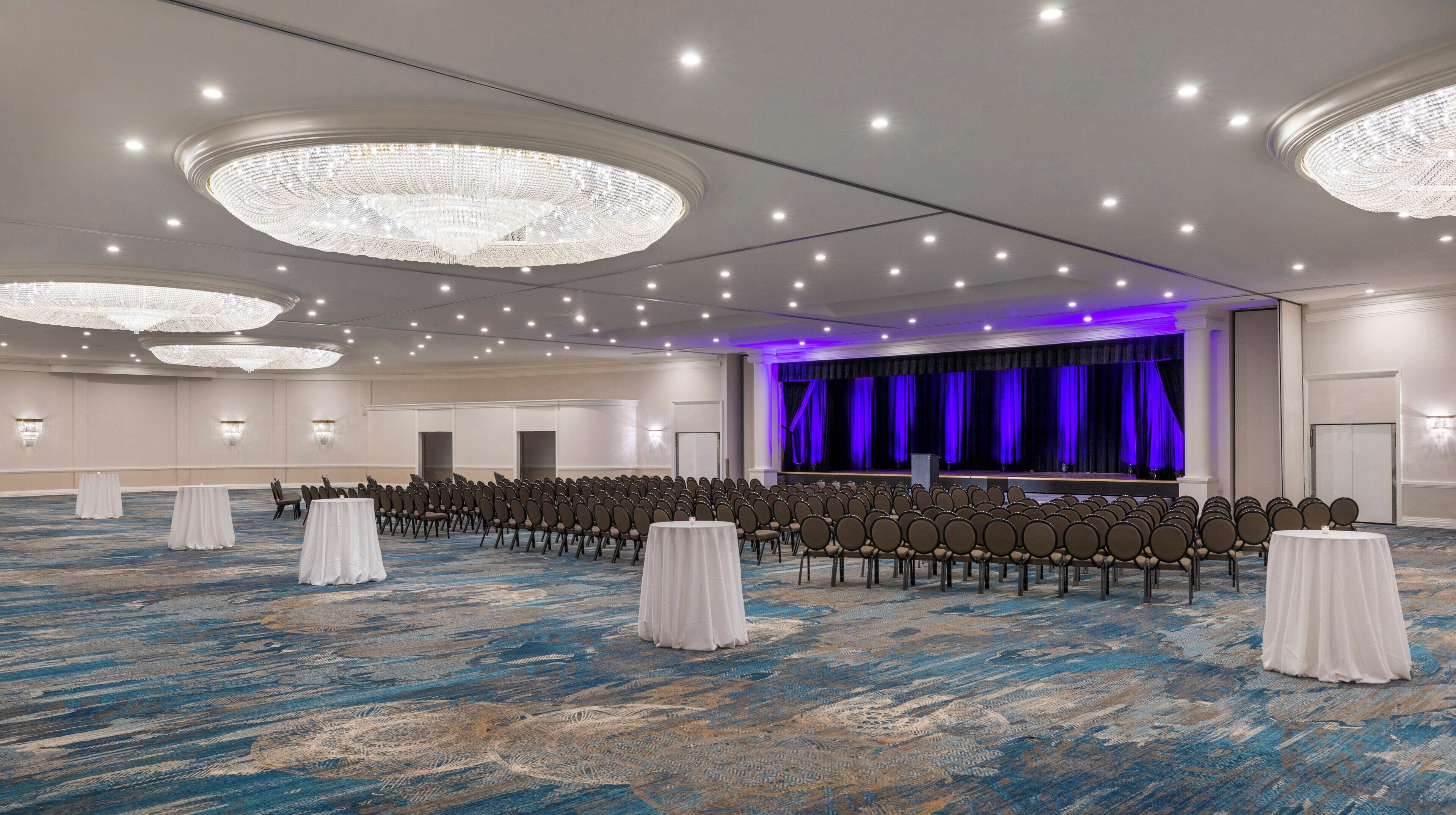 Un'ampia sala conferenze con file di sedie, un palco con tende e lampadari.