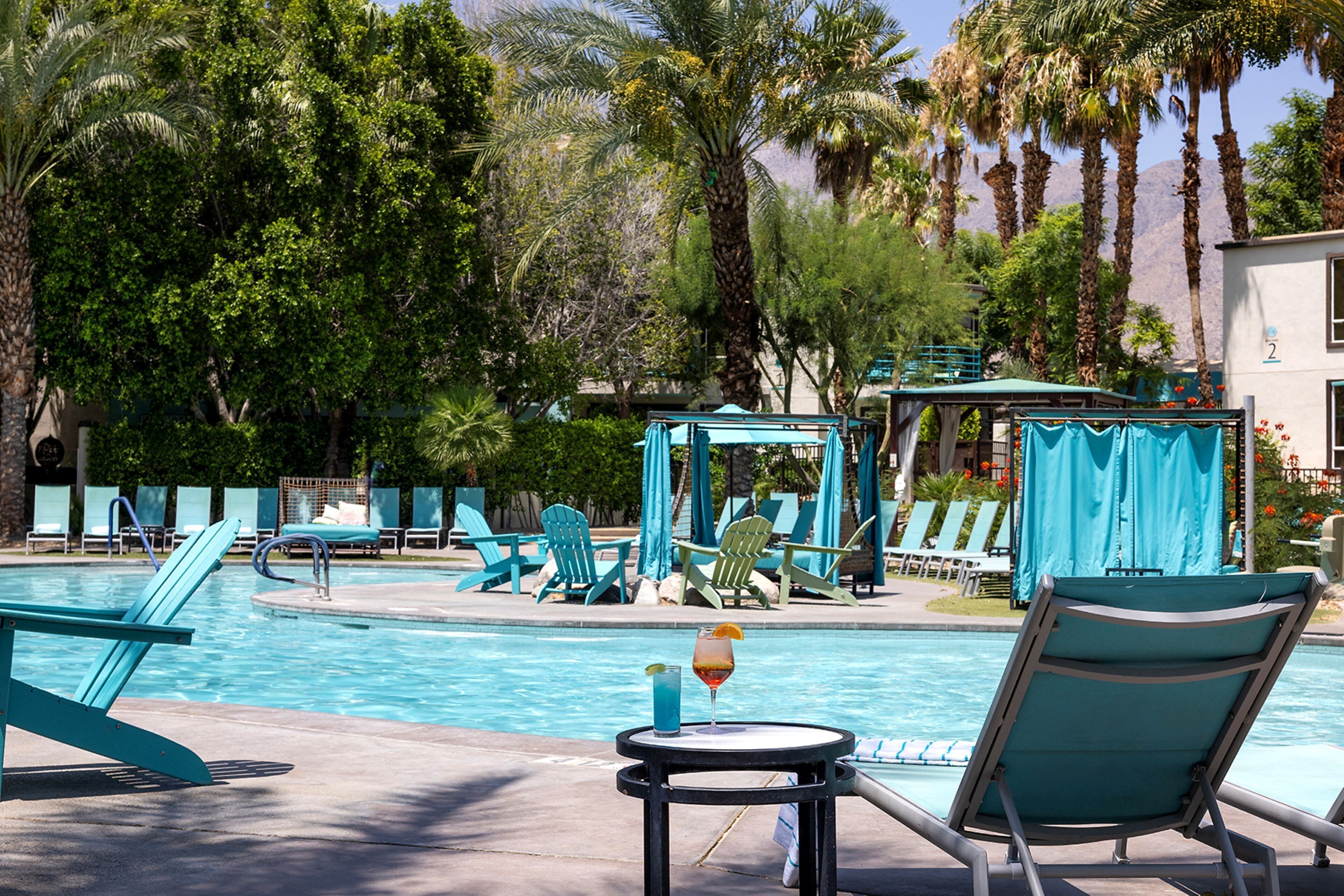 A pool area with lounge chairs, a small table with a drink, and a building in the background.