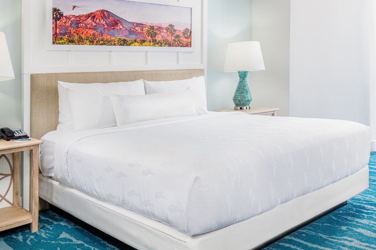 Habitación de hotel con una cama grande, dos mesitas de noche, un cuadro en la pared y una alfombra azul.