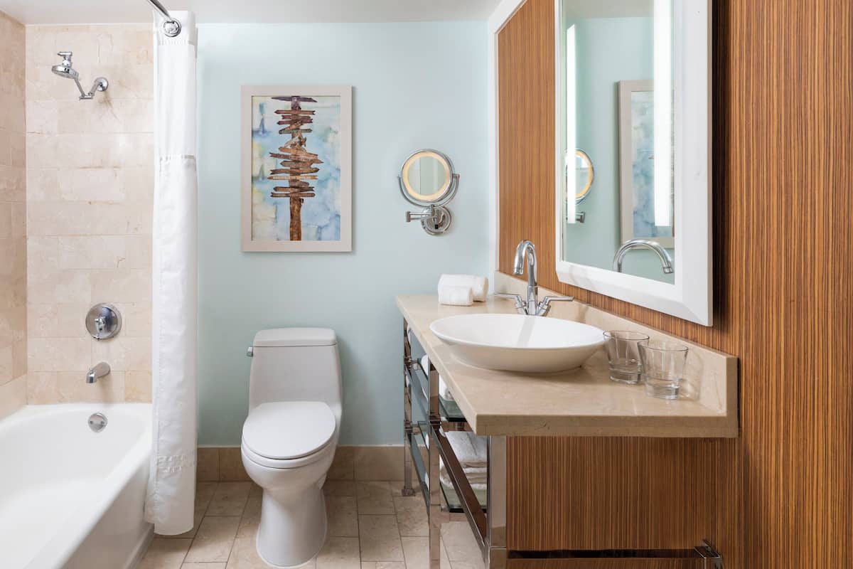 Un baño moderno con bañera, inodoro, tocador con lavamanos y un espejo grande.