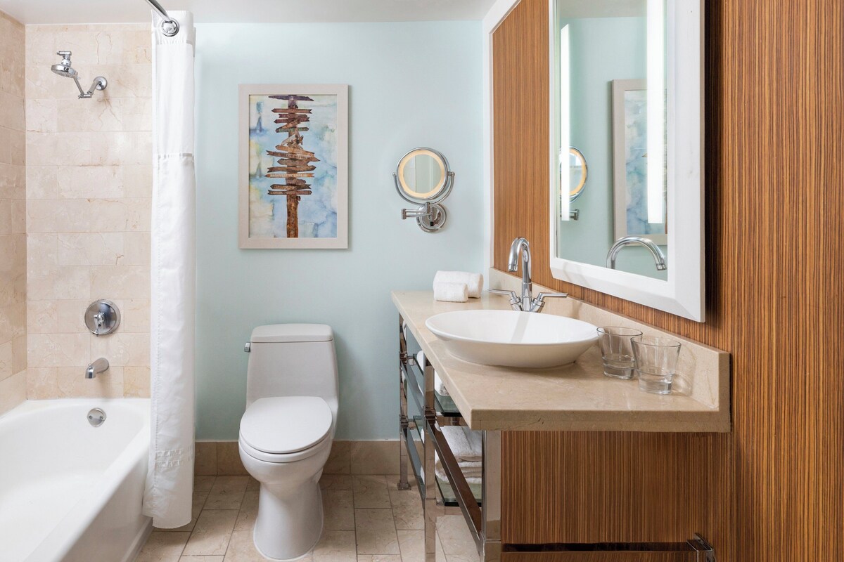 Un baño moderno con bañera, inodoro, tocador con lavamanos y un espejo grande.