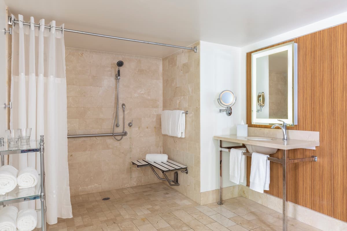 Un baño con ducha, lavabo, espejo y toallero.