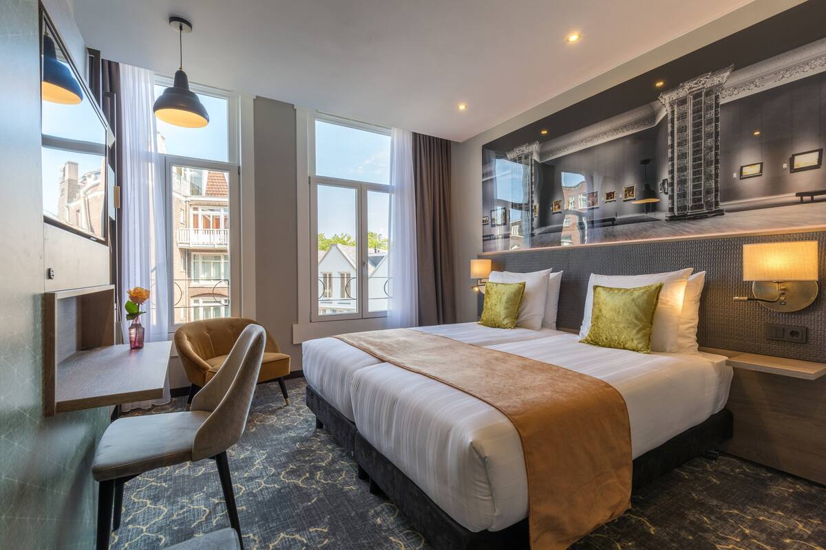 A hotel room with a large bed, a desk, a chair, and a view of the city.