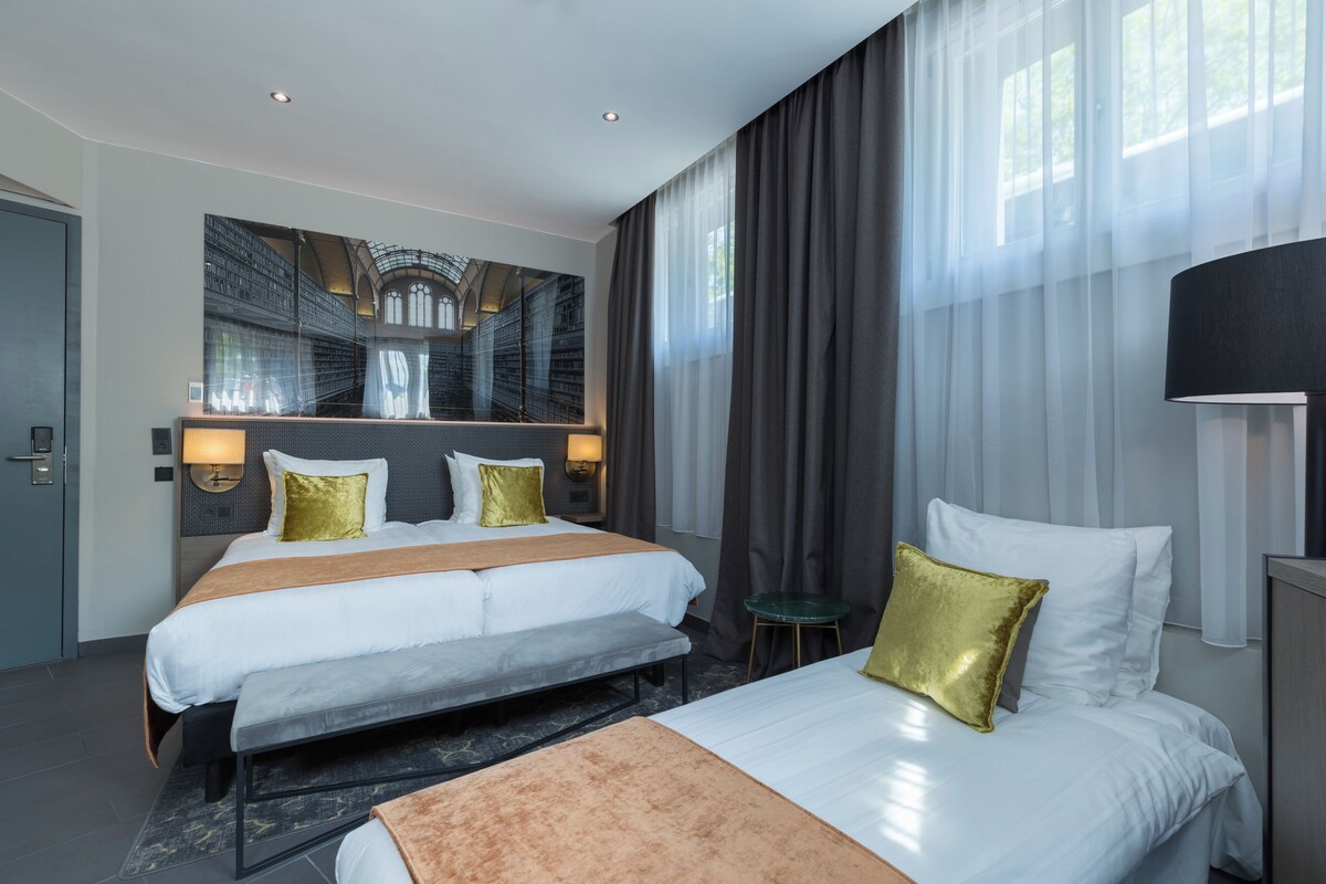 A hotel room with two beds, a large mirror, and a view of a library.