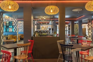 L’intérieur d’un restaurant avec un bar, des chaises rouges et blanches, et des luminaires suspendus.