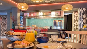 Una escena de desayuno con diversos pasteles, una jarra de jugo de naranja y una mesa de comedor con cubiertos.