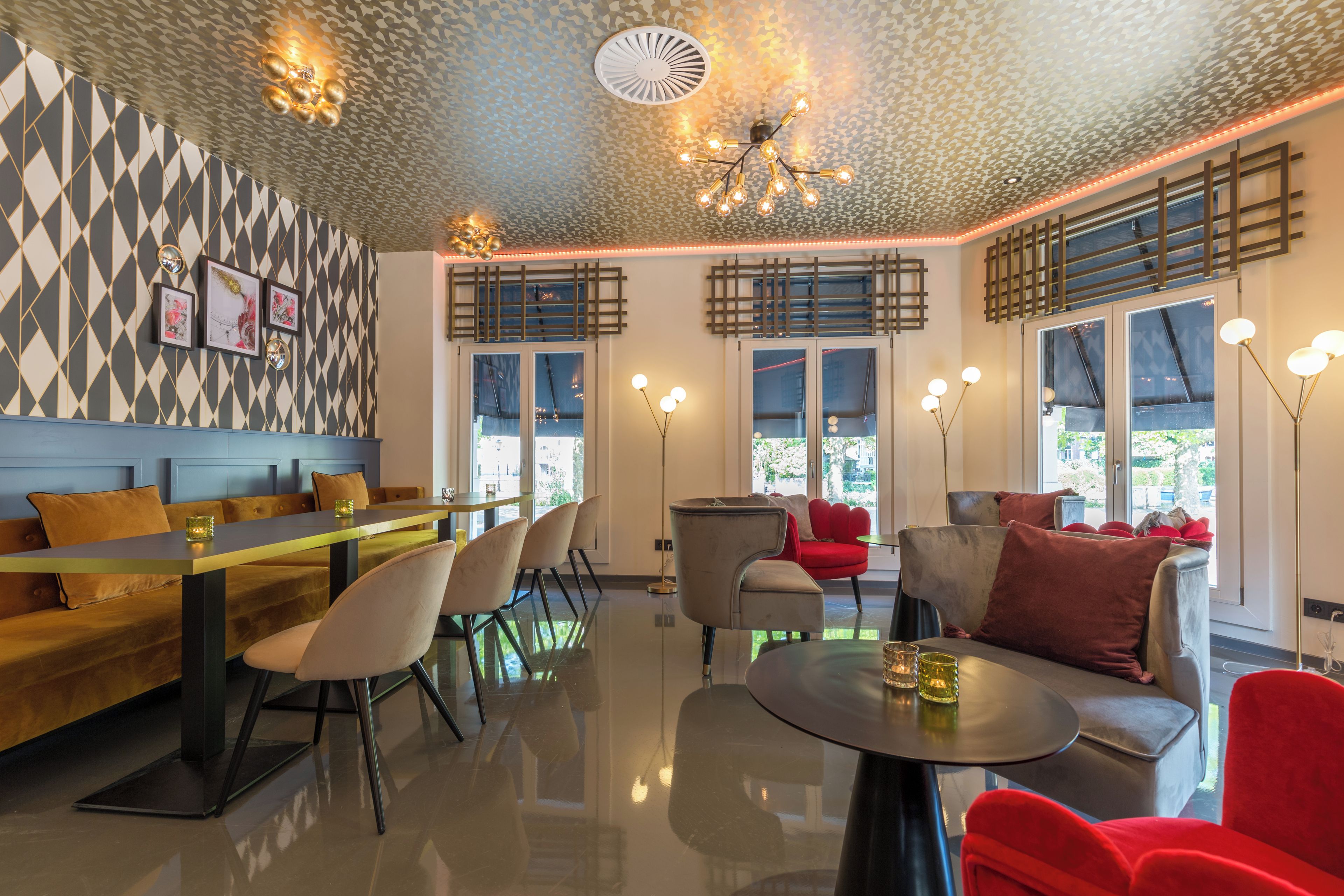 Un interior moderno con una pared de diseño geométrico, una zona de comedor con una mesa larga y sillas, un área de estar con sofás y una mesa redonda, y un techo con una lámpara original.