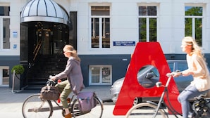 A building with a prominent dome entrance, a sign reading "PIETER CORNELIS HOFT" and "Museumkwater ZUID," and a red A-shaped structure on the sidewalk.