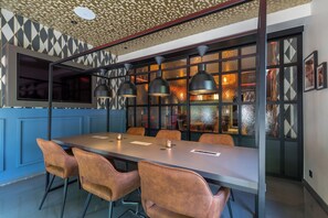 Un espace de salle à manger moderne, avec une longue table, de nombreuses chaises, des luminaires suspendus et un plafond à motifs.