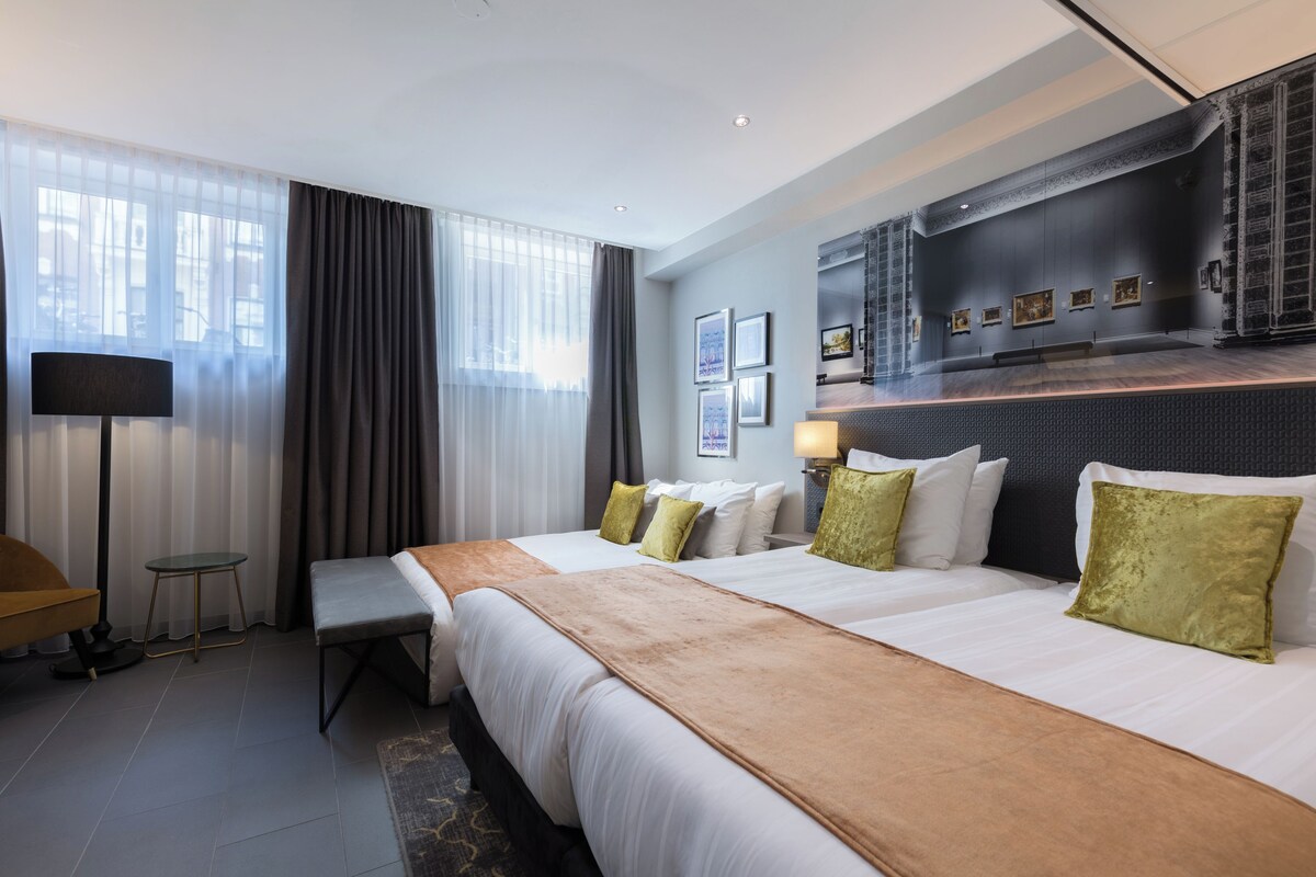 A hotel room with a large bed, a desk, a chair, a small table, and a wall-mounted TV.