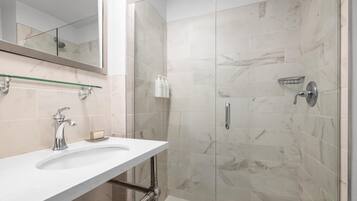 Un baño moderno con cabina de ducha de vidrio, un lavamanos blanco con encimera de mármol y un espejo grande sobre el lavamanos.
