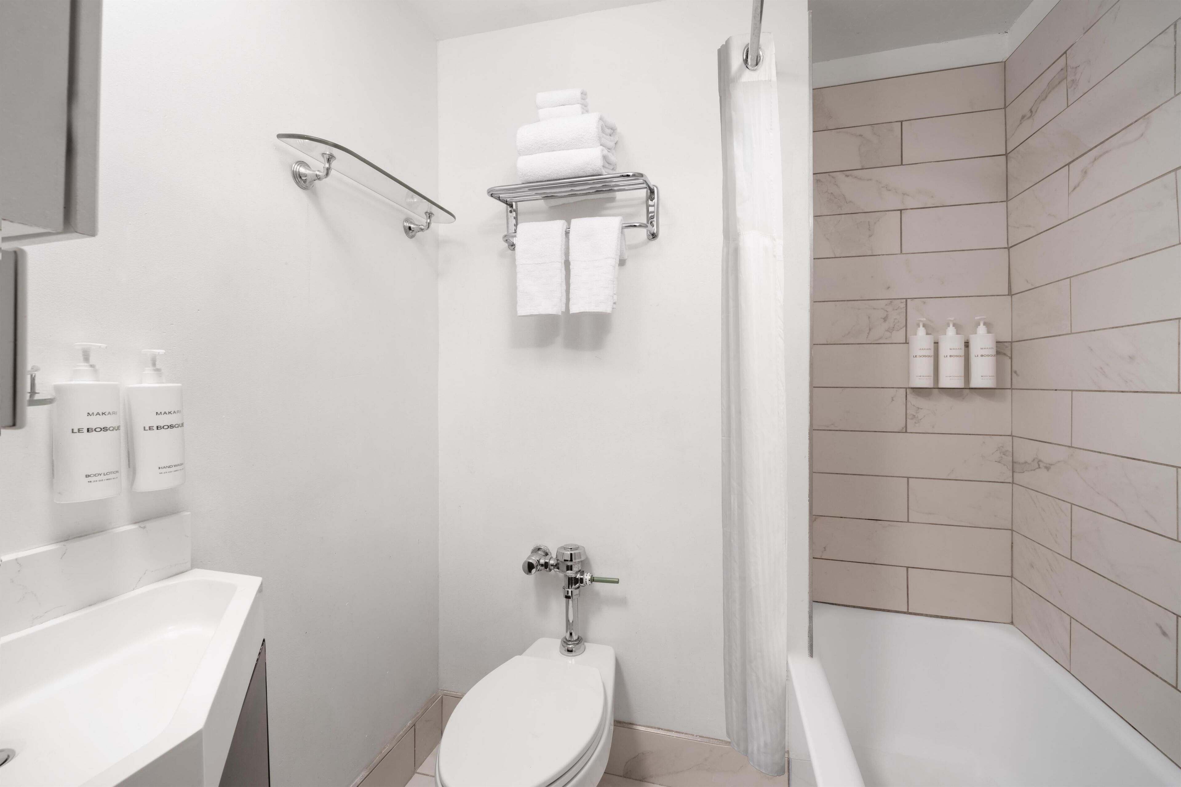 A modern bathroom with a toilet, sink, shower, and towel rack.