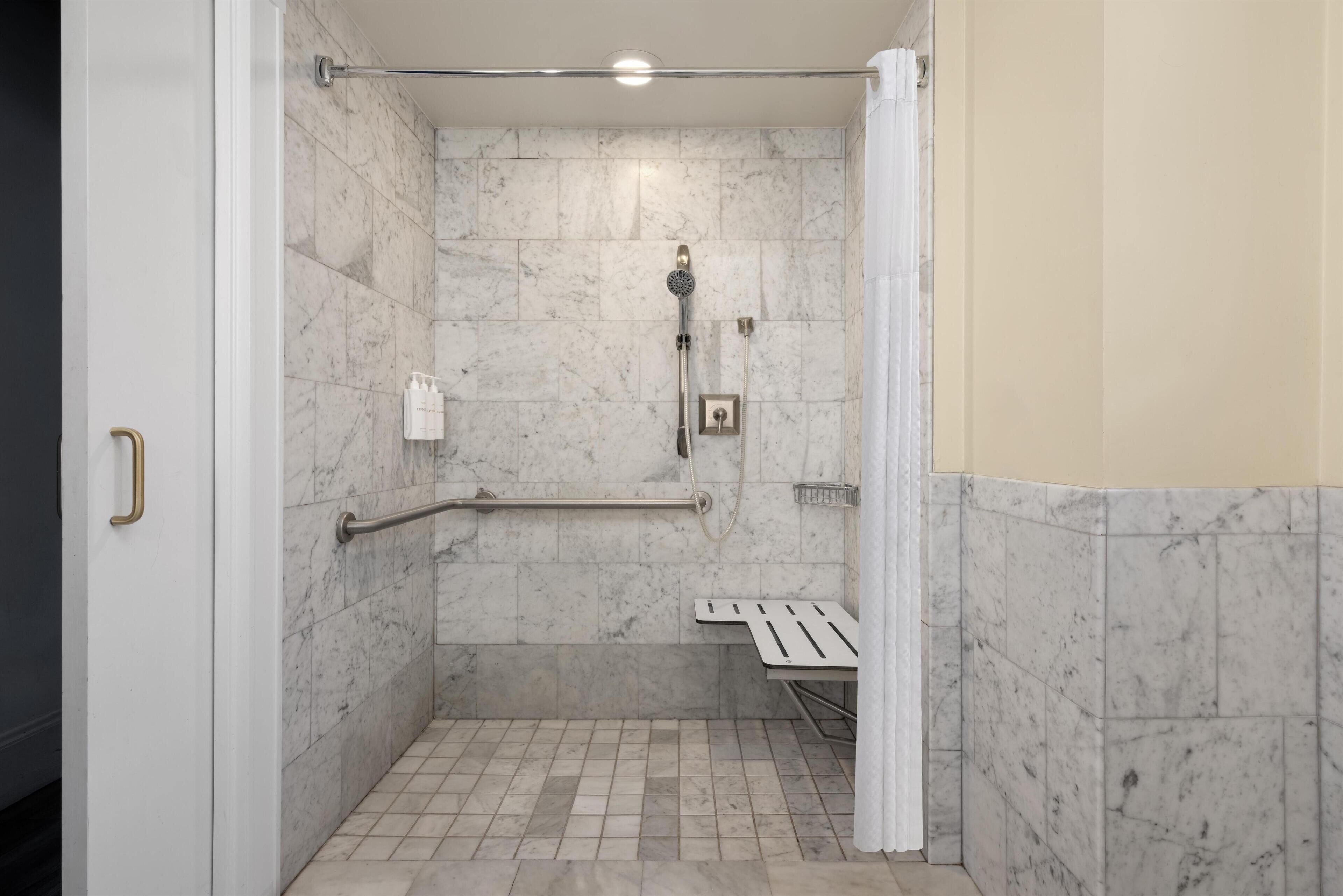 Une douche à l’italienne équipée d’une barre d’appui, d’un banc et d’un pommeau de douche.