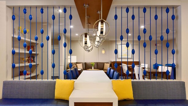 Un moderno vestíbulo de hotel con una zona de estar central, un comedor y una recepción.