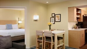 Una habitación de hotel con una cama, un escritorio con sillas, una pequeña kitchenette y un tapete azul a rayas.