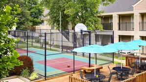 Un patio con cancha de baloncesto, mobiliario exterior y área de juegos cercada.