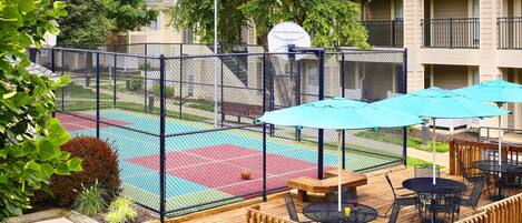 Une cour comprenant un terrain de basket, des sièges extérieurs et un espace de jeux délimité par une clôture.