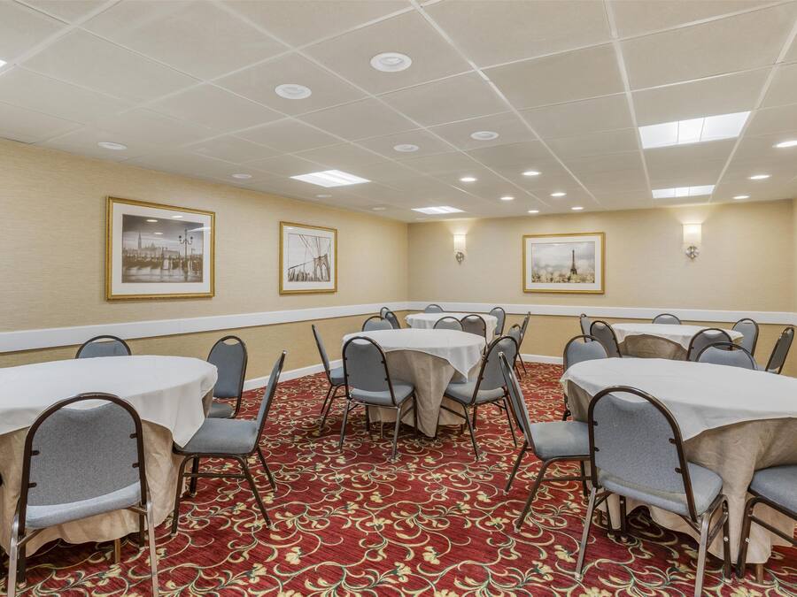 A conference room with round tables and chairs, beige walls, and framed pictures on the walls.