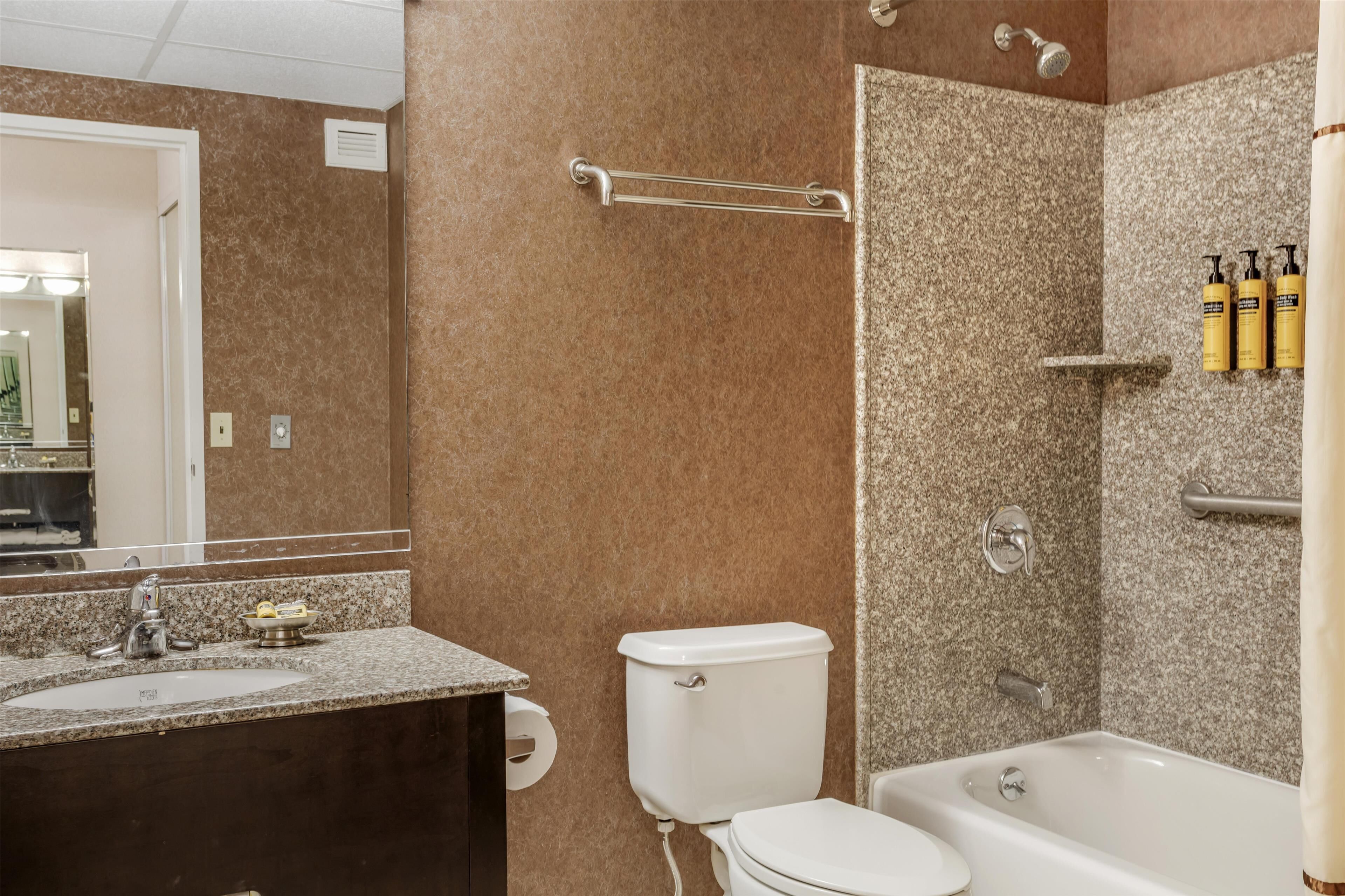 Un baño con lavamanos de encimera de granito, inodoro, bañera y ducha con toallero.