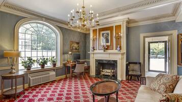 A room with a fireplace, a large window, a chandelier, and a red patterned carpet.
