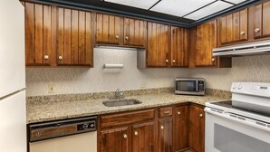 A kitchen with wooden cabinets, a granite countertop, a built-in microwave, and a dishwasher.
