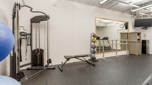Una palestra con attrezzature per esercizi, uno specchio, un orologio e una televisione appesa al muro.