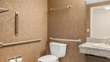 A bathroom with a toilet, grab bars, a sink, and a mirror.