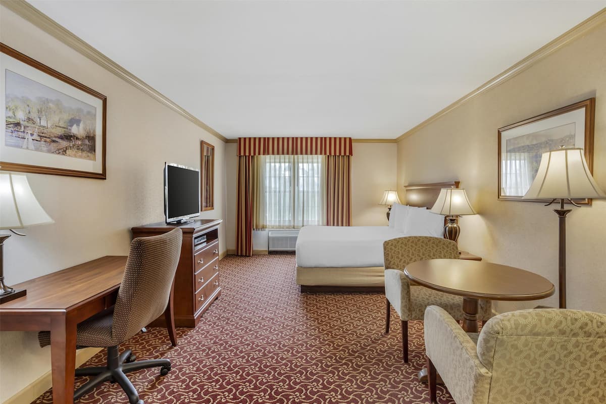A hotel room with a bed, desk, chair, television, and two lamps.